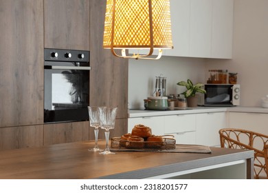 Wooden island table with delicious cinnamon rolls and wine glasses in modern kitchen at evening - Powered by Shutterstock