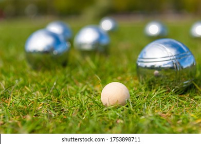 Wooden Jack On Green Lawn With Blurred Metal Bocce Balls In Background. 