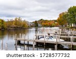 Wooden jetties on a river on a cloudy autumn day. Some waterside apartment buildings are visible among colouful autumnal trees on the other side of the river. Wolfeboro, NH. USA.