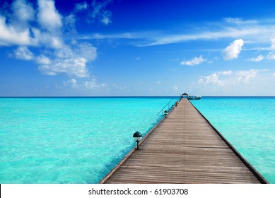 Wooden Jetty Over The Beautiful Maldivian Sea With Blue Sky