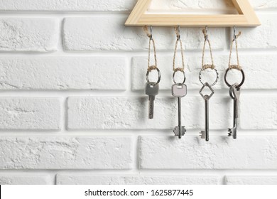 Wooden key holder on white brick wall indoors, closeup. Space for text