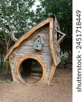 A wooden kids playhouse with sharp roof and a round opened door