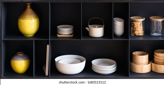 Wooden Kitchen Cabinet Cupboard With Many White And Clean Ceramic Dishes, Plates And Cups, Yellow Ceramic Jars All Neatly Cleaned Up In Black Color Shelves Modern Home Interior Showcase In Living Room