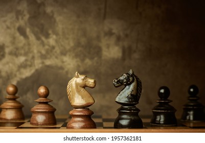 Wooden knights chess pieces facing each other on a vintage chessboard with pawns in the background. Rivalry concept, textured background.