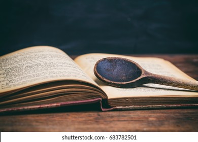 Wooden Ladle And A Vintage Cookbook On A Kitchen Table, Closeup View
