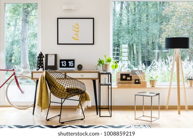 Wooden lamp and stool next to a desk with computer and metal chair in workspace with bike - Powered by Shutterstock