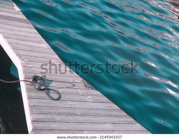 Wooden landing stage on blue water background.\
Boat knot equipment. Mooring knot, hitch on wooden desk. Travel and\
lifestyle view. Rigging equipment. Boat bridge on river Spree,\
Berlin. Vintage tones.