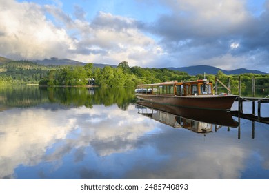 Wooden launch cruise boat moored next to jetty with reflections at Derwentwater on a calm Summer morning. Lake District, UK. - Powered by Shutterstock