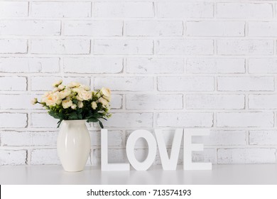 wooden letters forming word LOVE and flowers over white brick wall background