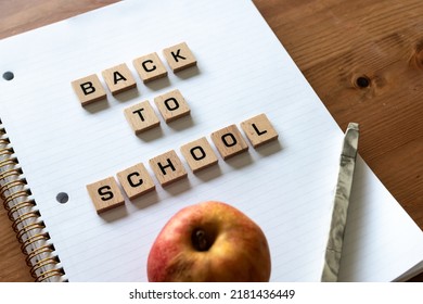 Wooden Letters Spell Out 'back To School' On A Blank White Lined Notepad Beside A Red Apple And A Pen. Hardwood Desk Surface. Back To School, In-person Learning, Online Learning, Studying, No People.