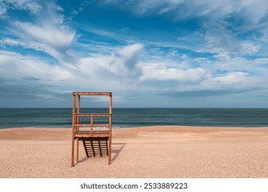  A wooden lifeguard tower stands solitary on a vast sandy beach, overlooking the calm blue Atlantic ocean under a partly cloudy sky. Serene and peaceful coastal scene - Powered by Shutterstock