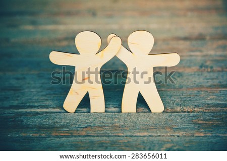 Wooden little men holding hands on wooden boards background. Symbol of friendship, love and teamwork