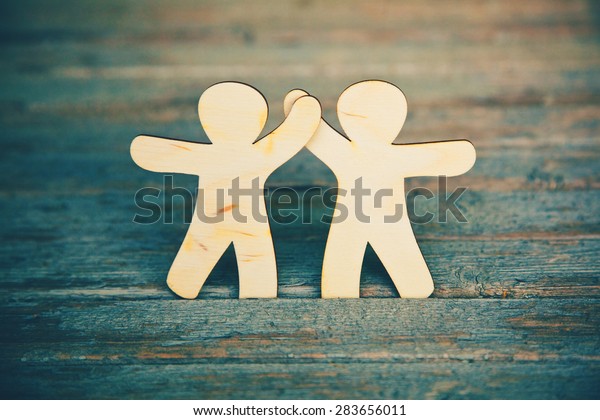 Wooden little men holding\
hands on wooden boards background. Symbol of friendship, love and\
teamwork