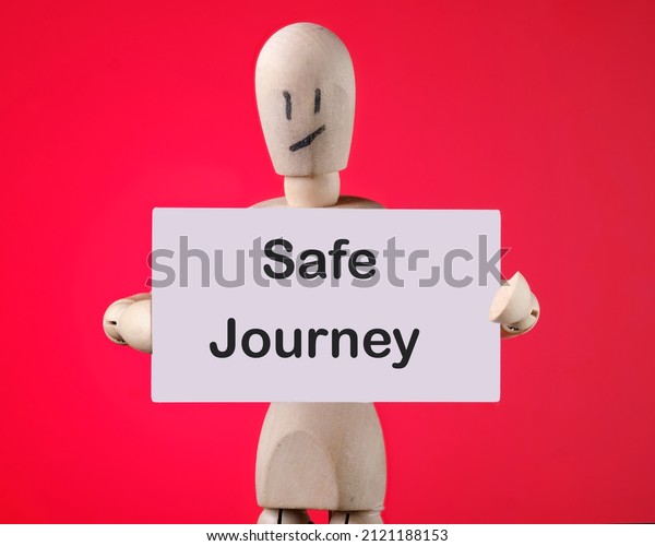 A\
wooden man holds a card with phrase Safe\
journey.