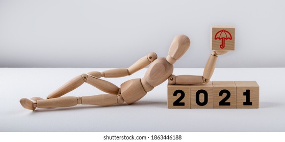 The wooden man lies next to the wooden cubes. Lettering 2021 and umbrella. Insurance concept. - Powered by Shutterstock