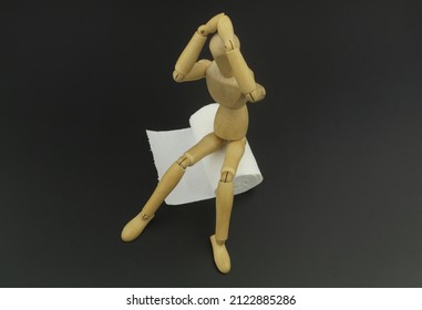 Wooden man mannequin figure sitting on roll of toilet paper on black background. Concept of problem with diarrhea, abdominal pain, food poisoning, intestinal infection.