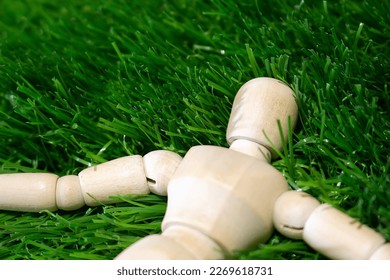 A wooden man puppet lies on the green grass with his arms outstretched. Wooden mannequin among green grass. - Powered by Shutterstock