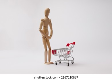a wooden man stands near an empty cart from a supermarket and wants to piss in it on a white background