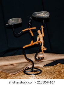 Wooden manikins on under a rock posing upside down  in different positions . The manikins are handing on a black figurine balancing the manikins.