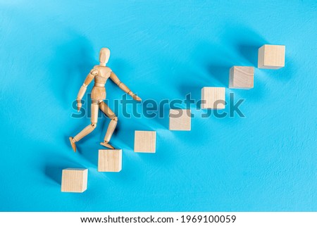 wooden mannequin climbing a ladder on blue background
