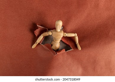 Wooden Mannequin Climbing Through A Hole In Red And Brown Decorative Paper