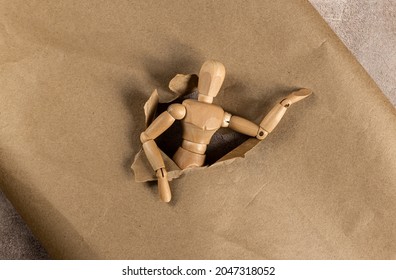 Wooden Mannequin Climbing Through A Hole In Decorative Paper