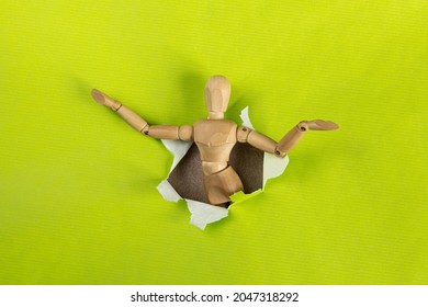 Wooden Mannequin Climbing Through A Hole In Green Decorative Paper