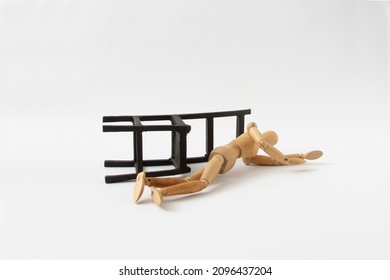 A wooden mannequin fell from a black chair on a white background. The minimal concept of a person who has fallen or is under the influence of alcohol. Drunkenness or fainting. - Shutterstock ID 2096437204