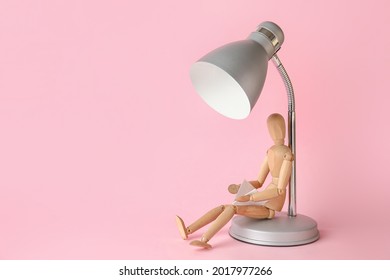 Wooden mannequin with lamp reading book on color background - Powered by Shutterstock