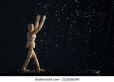 Wooden mannequin of a man in the rain pulls his hands up on a black background. The concept of joy. A wooden figure walks through puddles. - Powered by Shutterstock