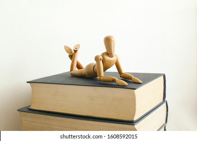 Wooden mannequin manikin lie down and rest on the books. He is thinking of mastering the material. A metaphor for rest after learning. Bad student. Disinterest in learning. Education. White background - Powered by Shutterstock