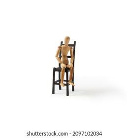 A wooden mannequin sits on a black chair on a white background. A minimal conception of a person who is exhausted, tired, depressed, desperate. - Powered by Shutterstock