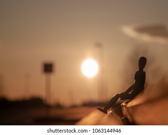 Wooden mannequin sitting on a wooden bench at sunset
