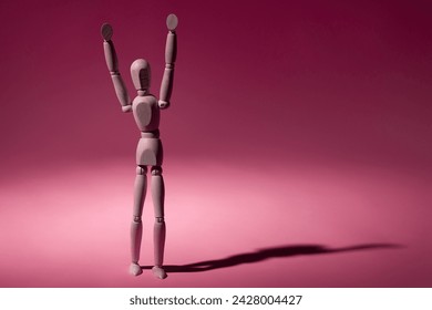 Wooden mannequin standing with arms raised, long shadow on a pink background. - Powered by Shutterstock