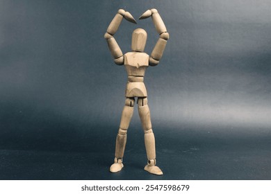 a wooden mannequin standing, his hands up in a heart symbol - Powered by Shutterstock