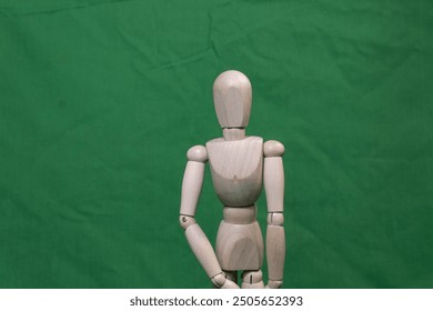 A wooden mannequin stands in a neutral pose against a green background. The simple composition highlights the mannequin's form, ideal for artistic or educational purposes. - Powered by Shutterstock