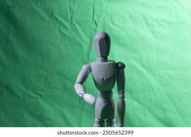 A wooden mannequin stands in a neutral pose against a green background. The simple composition highlights the mannequin's form, ideal for artistic or educational purposes. - Powered by Shutterstock