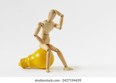 Wooden mannequin in thinking pose sitting on yellow light bulb - Concept of ideas and creative thinking - Powered by Shutterstock