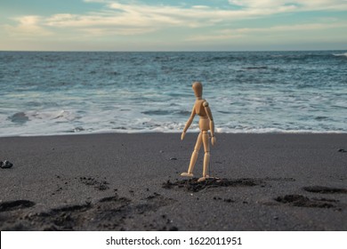 A wooden mannequin walks along the beach with black sand - Powered by Shutterstock