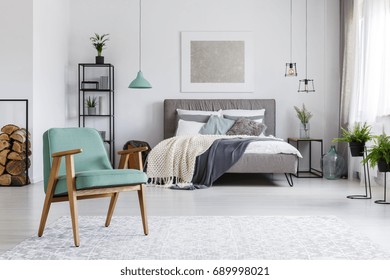 Wooden mint armchair standing on a bright carpet in cozy room with bed