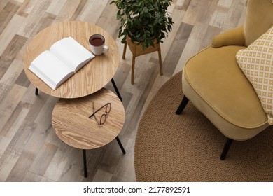 Wooden nesting tables near houseplant and armchair in room. Interior design