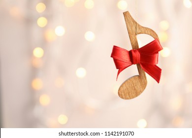 Wooden Note With Bow Against Blurred Lights. Christmas Music Concept