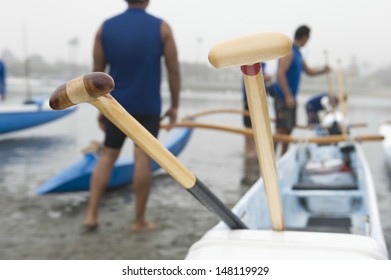 Wooden oars on outrigger canoe with canoeists in background at beach