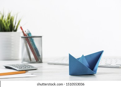 Wooden Office Desk With Deep Blue Origami Boat. Individual Banking And Money Saving. Flat Lay Office Workplace With Plant In Pot, Computer Keyboard And Calculator. Creative Company Marketing Concept