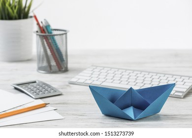 Wooden Office Desk With Deep Blue Origami Boat. Individual Banking And Money Saving. Flat Lay Office Workplace With Plant In Pot, Computer Keyboard And Calculator. Creative Company Marketing Concept