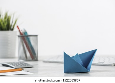 Wooden Office Desk With Deep Blue Origami Boat. Individual Banking And Money Saving. Flat Lay Office Workplace With Plant In Pot, Computer Keyboard And Calculator. Creative Company Marketing Concept