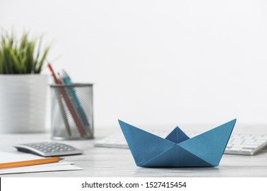 Wooden Office Desk With Deep Blue Origami Boat. Individual Banking And Money Saving. Flat Lay Office Workplace With Plant In Pot, Computer Keyboard And Calculator. Creative Company Marketing Concept