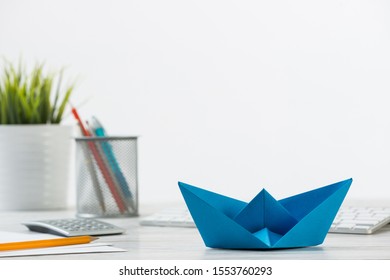 Wooden Office Desk With Deep Blue Origami Boat. Individual Banking And Money Saving. Flat Lay Office Workplace With Plant In Pot, Computer Keyboard And Calculator. Creative Company Marketing Concept