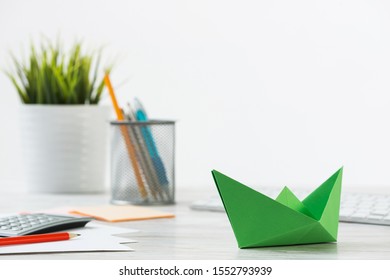 Wooden Office Desk With Green Origami Boat. Individual Investment And Money Saving. Flat Lay Office Workplace With Plant In Pot, Computer Keyboard And Calculator. Green Technologies And Innovations