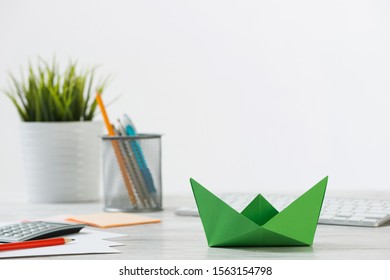 Wooden Office Desk With Green Origami Boat. Individual Investment And Money Saving. Flat Lay Office Workplace With Plant In Pot, Computer Keyboard And Calculator. Green Technologies And Innovations